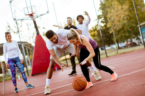 Group of multiracial young people   playing basketball outdoors