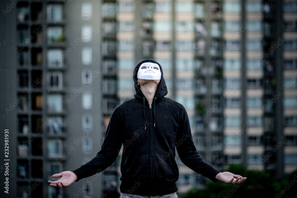 Mystery hoodie man in white mask standing in the rain looking up at the sky on rooftop of abandoned building. Bipolar disorder or Major depressive disorder. Depression concept