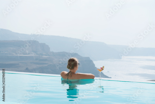 Young woman relaxing in the pool with a gorgeous view on Santorini.