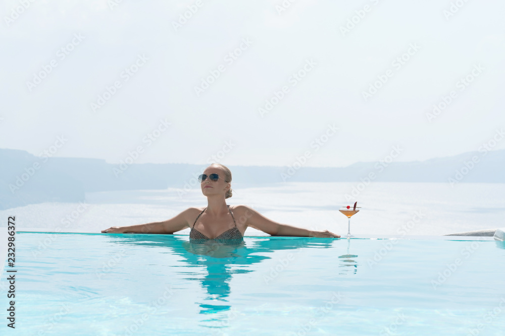 Young woman relaxing in the pool with a gorgeous view on Santorini.