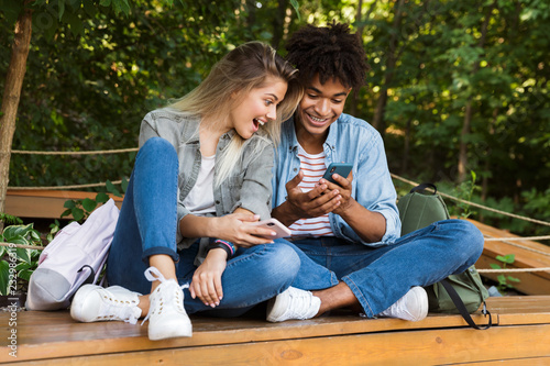 Happy young loving couple using mobile phone outdoors in park.