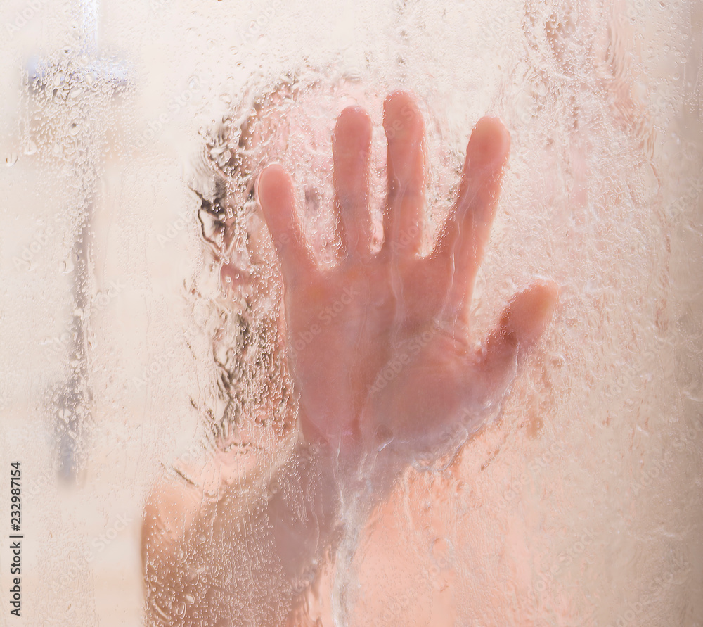 Fototapeta premium Female hand on the blurry glass of the shower door.