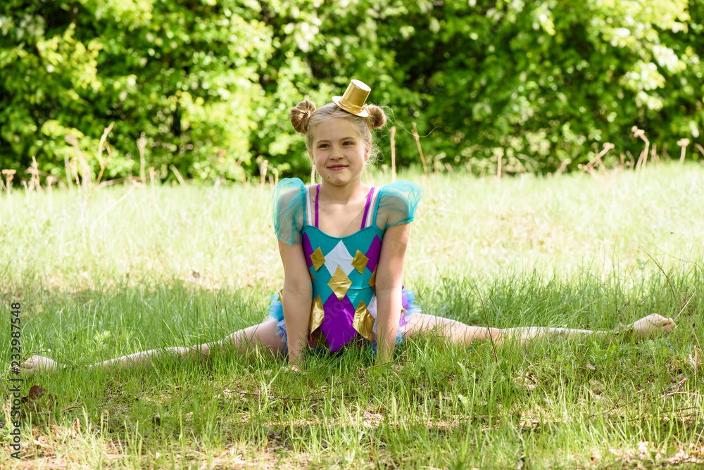 Young sporty blond girl sitting on grass in the park,gymnastic splits