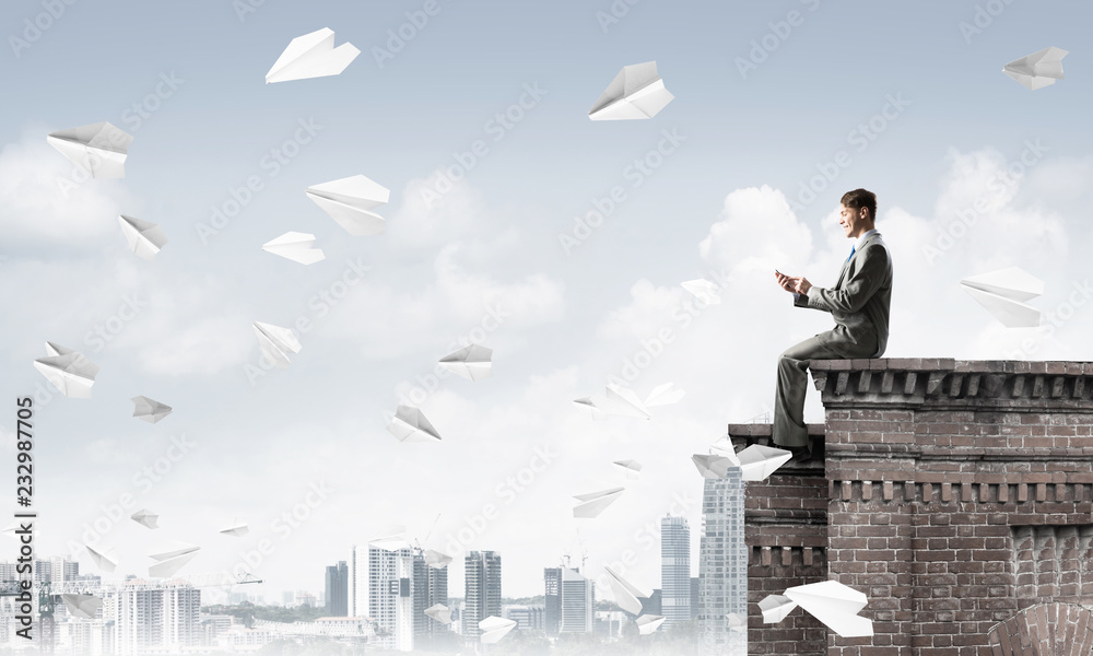 Businessman or student on roof edge making calls and cityscape at background Businessman or student on roof edge making calls and cityscape at background