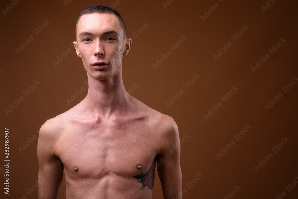 Fototapeta premium Young handsome androgynous man shirtless against brown backgroun