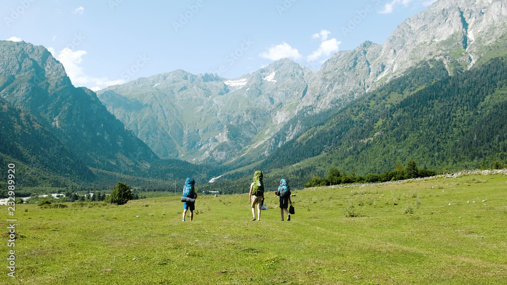 Tourists hikers with large backpacks are walking in the mountains in a hike against the backdrop of a beautiful landscape. Tourists hikers with large backpacks are walking in the mountains in a hike against the backdrop of a beautiful landscape.