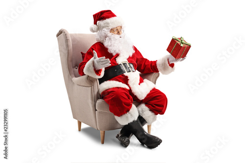 Santa Claus sitting in an armchair and holding a present