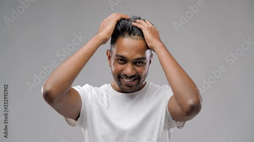 grooming, hairstyling and people concept - smiling young indian man applying hair wax or styling gel over gray background