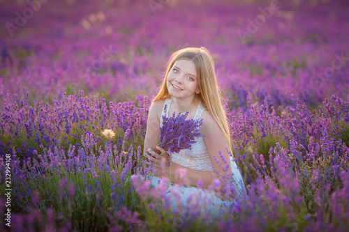 Smiling beautiful blond lady model on lavender field enjoy summer day wearing airy whit dress with bouquet of flowers.