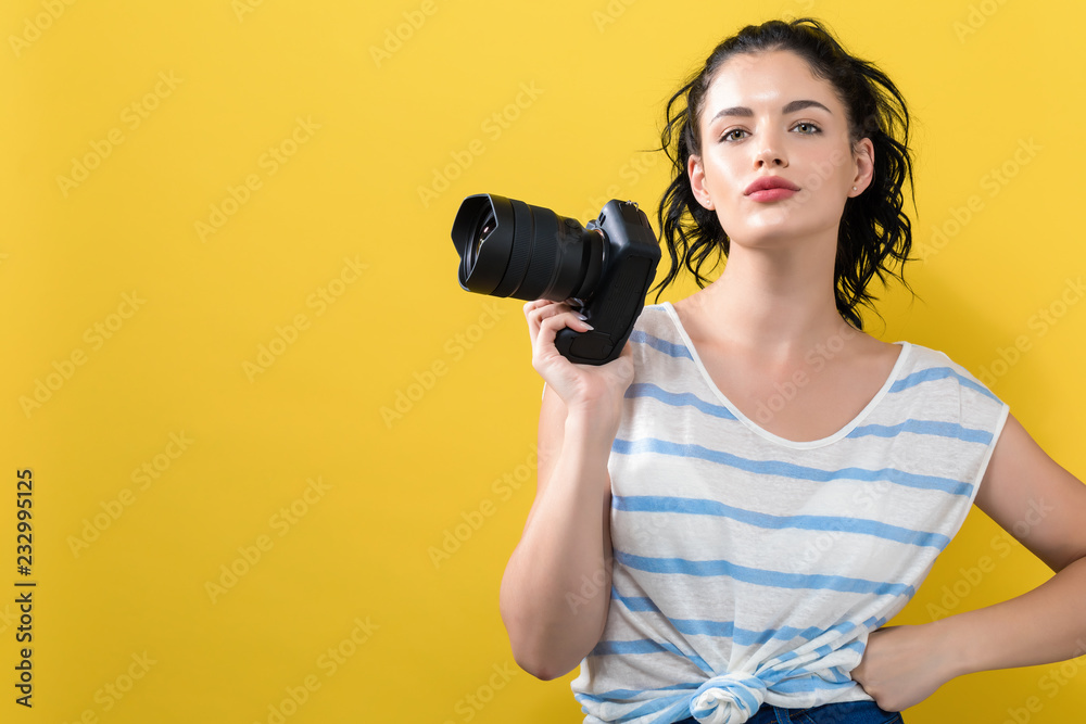 Young woman with a professional digital SLR camera on a yellow background Young woman with a professional digital SLR camera on a yellow background