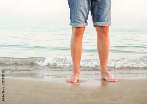 Mann am Strand am Meer steht mit nackten Beinen im Wasser