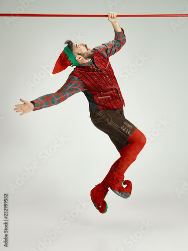 The happy smiling friendly man dressed like a funny gnome or elf hanging on an isolated gray studio background. The winter, holiday, christmas concept