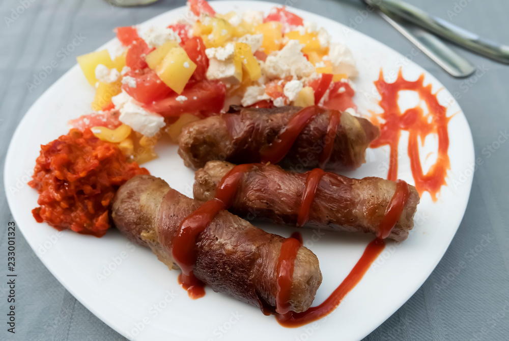 Chevapchichi. Meat sausages with vegetable salad, ketchup and adjika on white plate. Dish of Balkan cuisine.