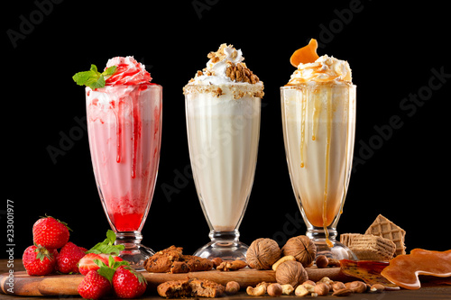 Three sweet milkshakes with nuts, caramel, strawberry and whipped cream at a wooden board on table background. photo