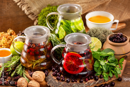 Three teapots with tea assortment decorated with nuts, citrus, black currant berries and mint at wooden table background.