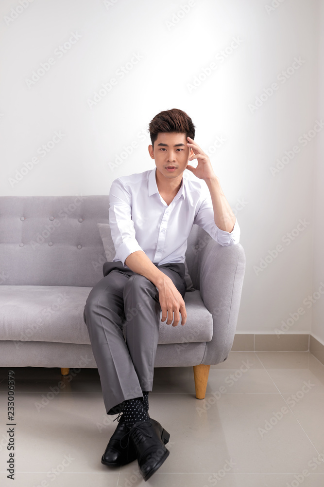 Vertical shot of a joyful businessman sitting on a couch and looking at the camera isolated on white background