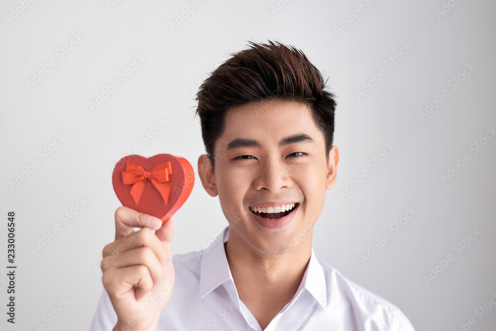 A gift for the beloved. Young beautiful smiling elegant man in a white shirt holding a box with a gift and shows it to the camera. Valentine's Day. A gift for the beloved. Young beautiful smiling elegant man in a white shirt holding a box with a gift and shows it to the camera. Valentine's Day.