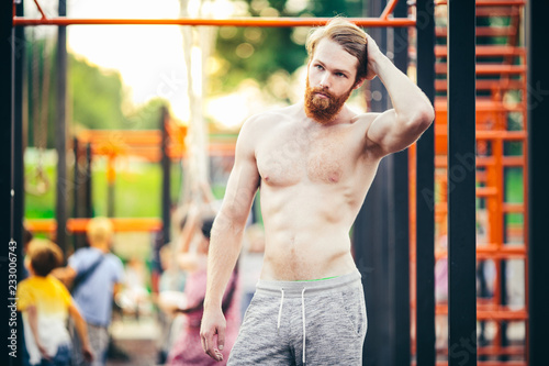 Photography A handsome young Caucasian man with a naked muscular torso with long red hair and a beard posing on a street sports field, an outdoor gym