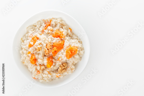 Oatmeal with pumpkin and nuts in a white plate on a white background. View from above. Copy space. Close-up