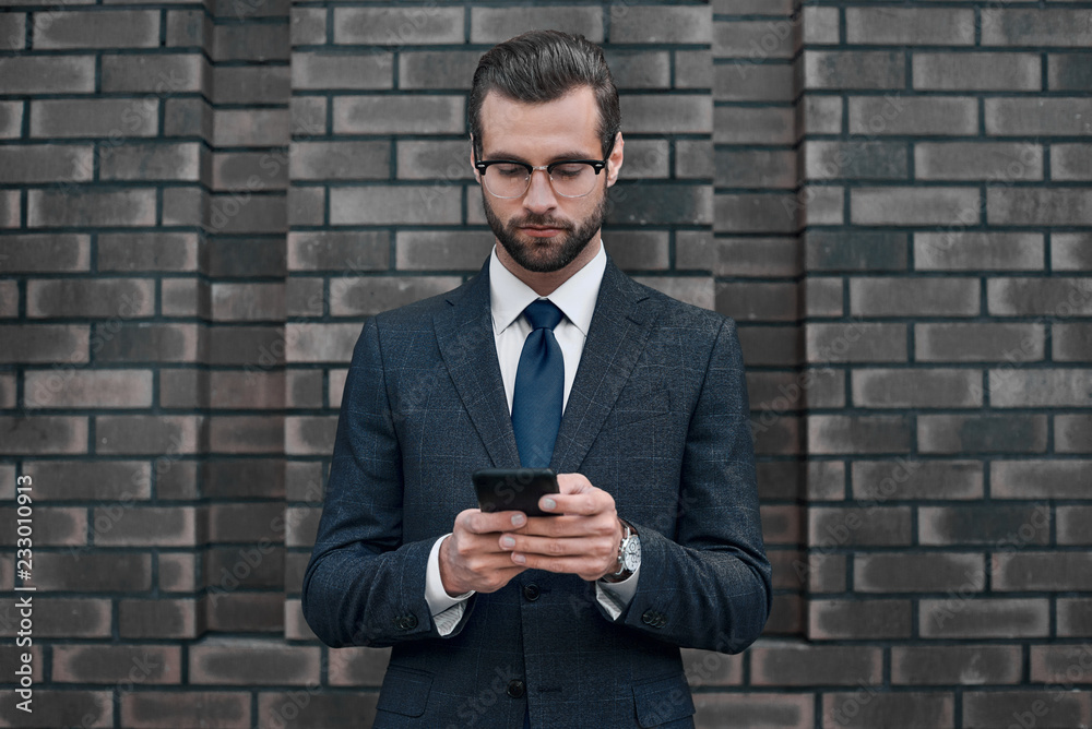 A young businessman in glasses and an expensive suit, works on a smarphone in his hands A young businessman in glasses and an expensive suit, works on a smarphone in his hands