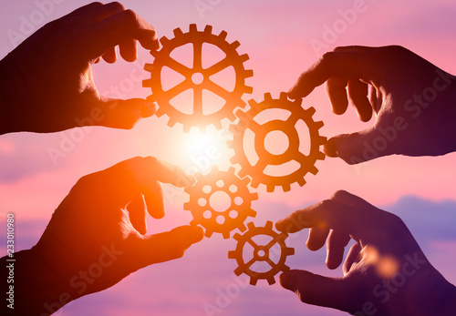 wooden gears in the hands of a group of people on the background of the evening sky. the concept of teamwork. mechanism.