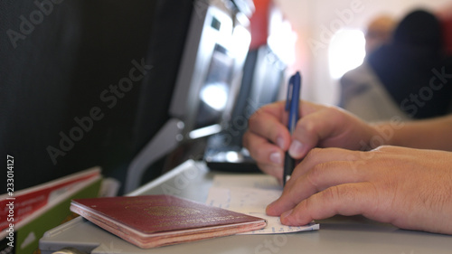 Passenger with passport is filling in the migration or arrival cards in the plane while flight