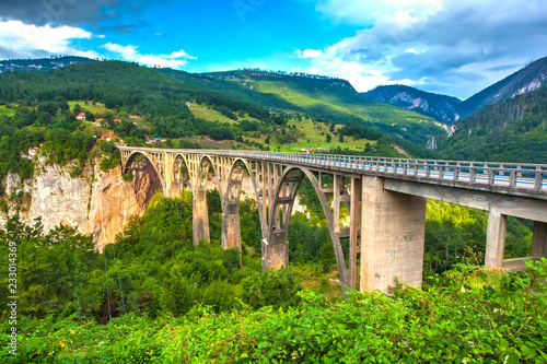 Fotografie Beautiful stone bridge with huge arches between rocky mountains with lush green forest over the deep canyon of the river