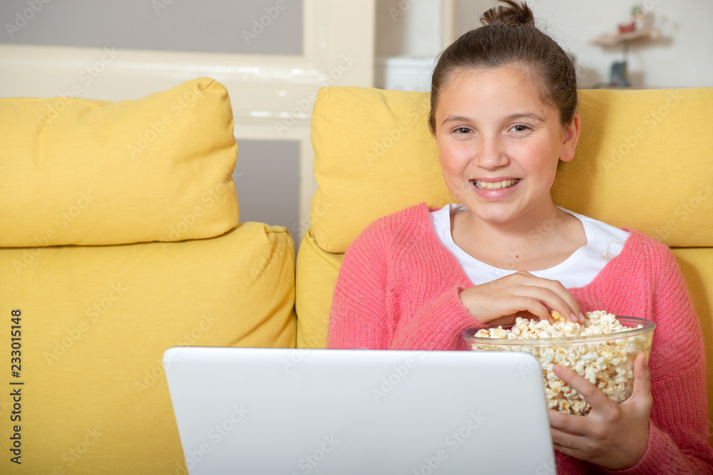 smiling teenage girl using laptop and eating popcorn