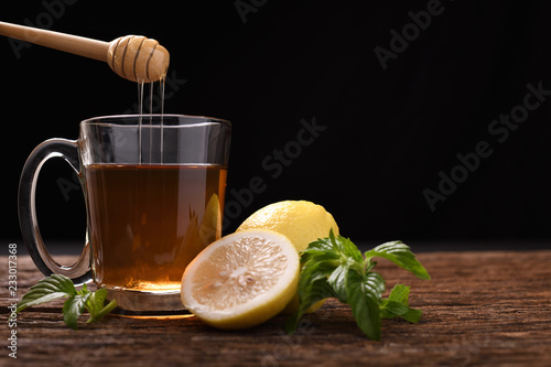 Hot honey lemon tea in glass with mint and sliced lemon on wooden table and black background