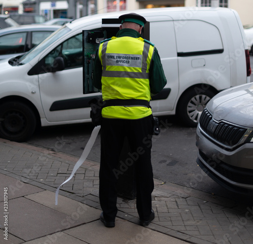 civil enforcement officer traffic warden tries to fix parking meter in busy high street photo