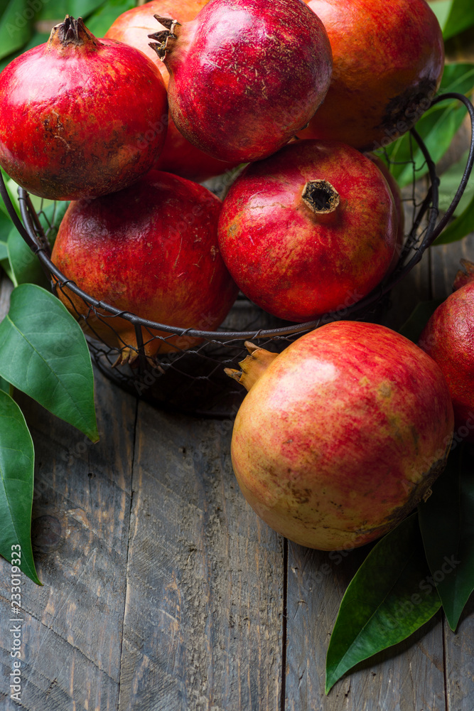 Ripe juicy organic bright red pomegranates in metal wicker basket with branches green leaves on plank barn wood background. Fall produce harvest vitamins abundance concept. Rosh Hashanah holiday Ripe juicy organic bright red pomegranates in metal wicker basket with branches green leaves on plank barn wood background. Fall produce harvest vitamins abundance concept. Rosh Hashanah holiday
