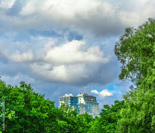 Modern city building among green trees and blue sky with large fluffy clouds
