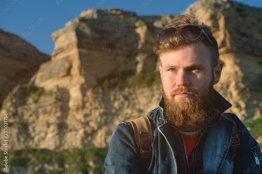 Close-up portrait of a bearded stylish traveler in a cap against epic rocks. Time to travel concept Close-up portrait of a bearded stylish traveler in a cap against epic rocks. Time to travel concept