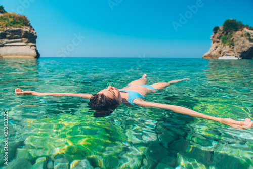 woman swimming on back in clear blue sea water.