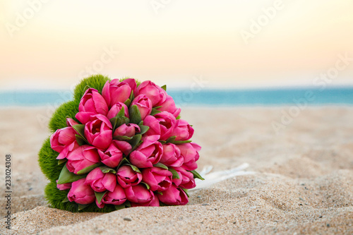 Fototapeta Naklejka Na Ścianę i Meble -  Bellissimo Bouquet di tulipani rosa, poggiato nella sabbia di una spiaggia, sfondo mare e cielo al tramonto