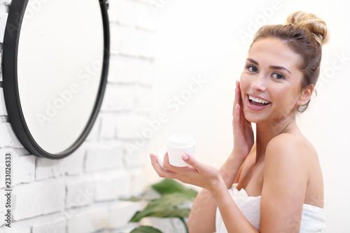 Young woman cleaning face in bathroom mirror