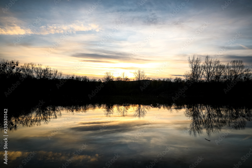 Obraz premium The lake during sunset looking at the water and the trees on the other side of the shadows.