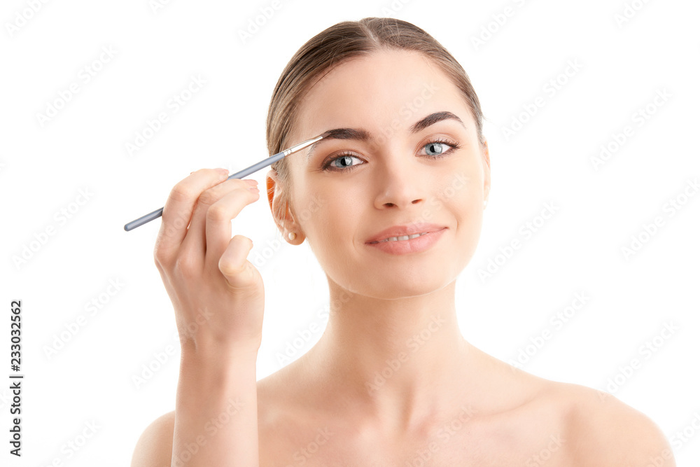 Studio shot of a beautiful young woman applying makeup to her eyebrow while standing at isolated white background. Studio shot of a beautiful young woman applying makeup to her eyebrow while standing at isolated white background.