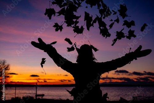 Woman throwing Fall Leaves in the sunset