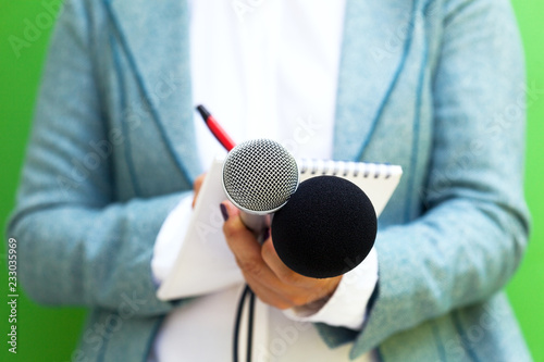 Female journalist at news conference, writing notes, holding microphone