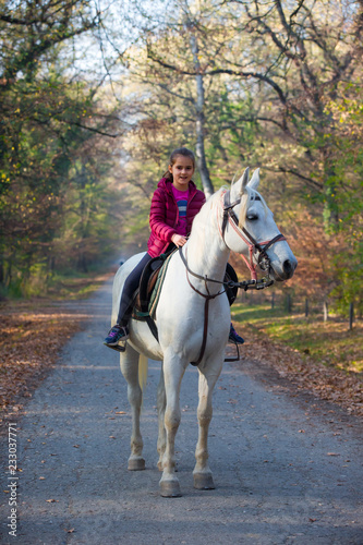 A girl rides a white horse in the forest