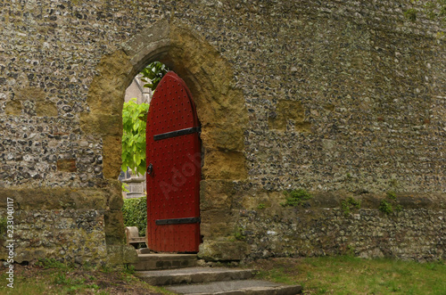 Rote geöffnete Tür in Mauerwand zu verstecktem Garten