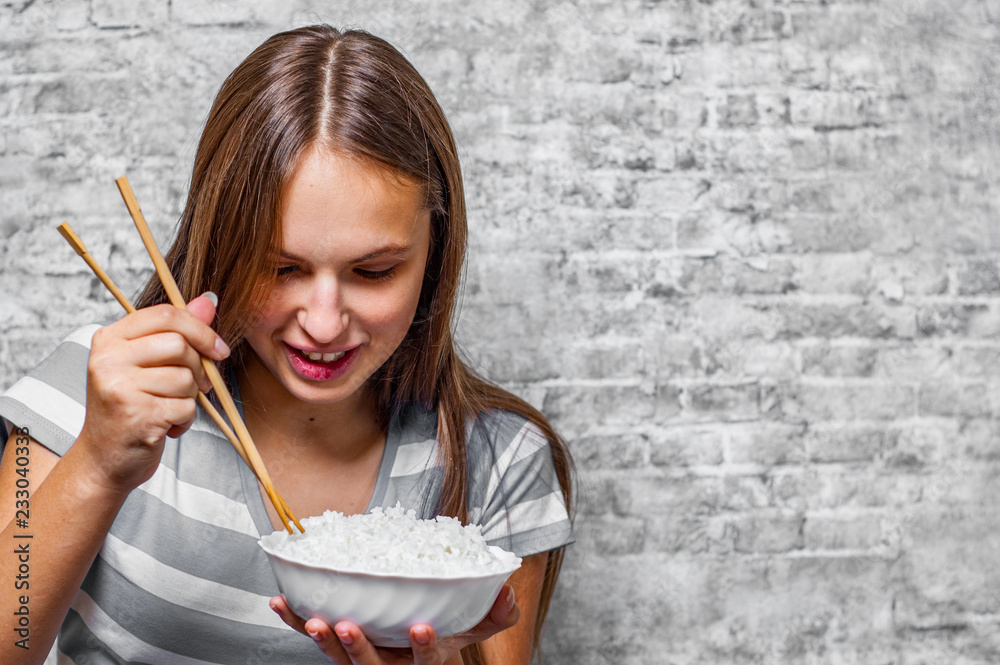 portrait of young teenager brunette girl with long hair eating rice on gray wall background portrait of young teenager brunette girl with long hair eating rice on gray wall background