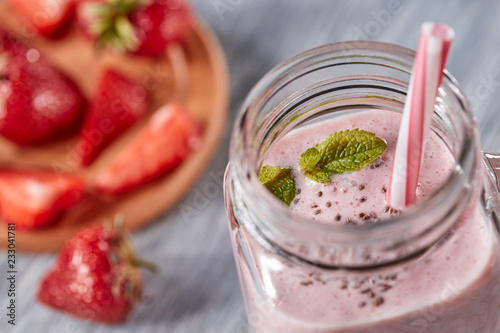 Closeup of organic milky strawberry smoothie with chia seeds and mint leaves in a glass with a straw on a wooden table. Healthy dessert. Top view