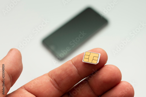 nano sim card on the finger on the background of the smartphone lying in the defocus, on a white background