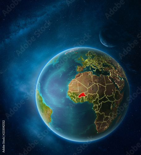 Planet Earth with highlighted Burkina Faso in space with Moon and Milky Way. Visible city lights and country borders.