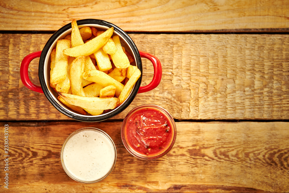 top view of delicious french fries in a red pot with sauces on an old wooden table top view of delicious french fries in a red pot with sauces on an old wooden table