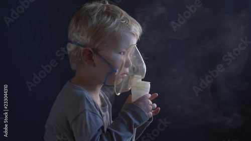 Caucasian blonde boy inhales couples containing medication from inhaler to stop coughing. Medical procedures. Inhaler. Respiratory medicine. Bronchitis, asthmatic health problem. Home treatment breath photo