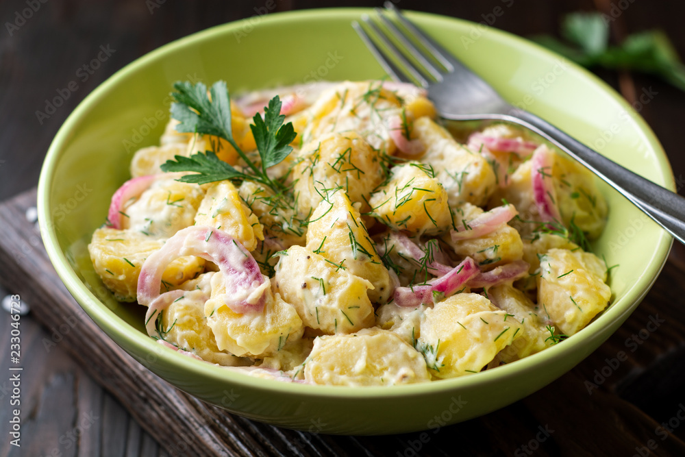 Potato salad with red onion and greens in bowl on dark wooden table. Selective focus.