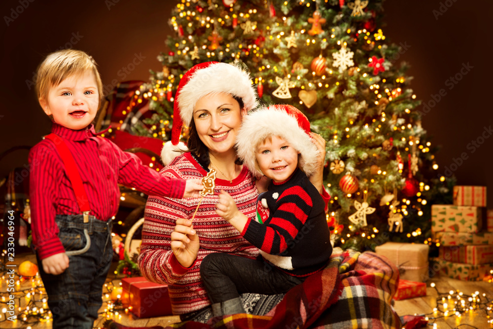 Christmas Family, Mother with Children front of Xmas Tree Lights, Happy Mom and Baby in Red Hat Christmas Family, Mother with Children front of Xmas Tree Lights, Happy Mom and Baby in Red Hat